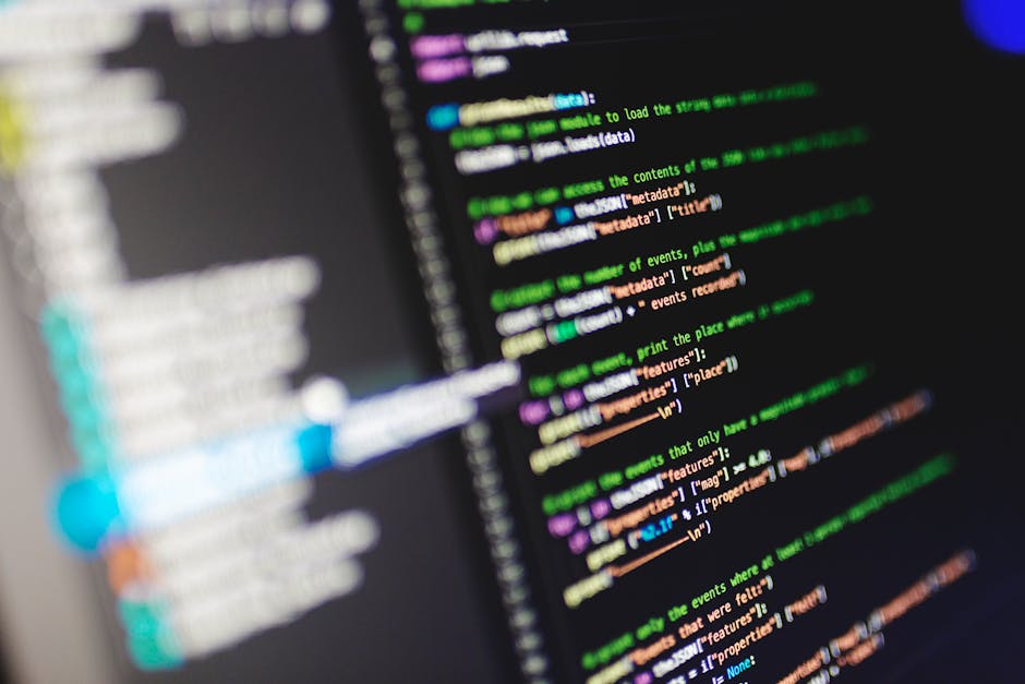 Photograph of a computer screen displaying lines of multicolored code in various shades of green, purple, orange, and blue against a dark background. The code appears to be part of a programming or sc